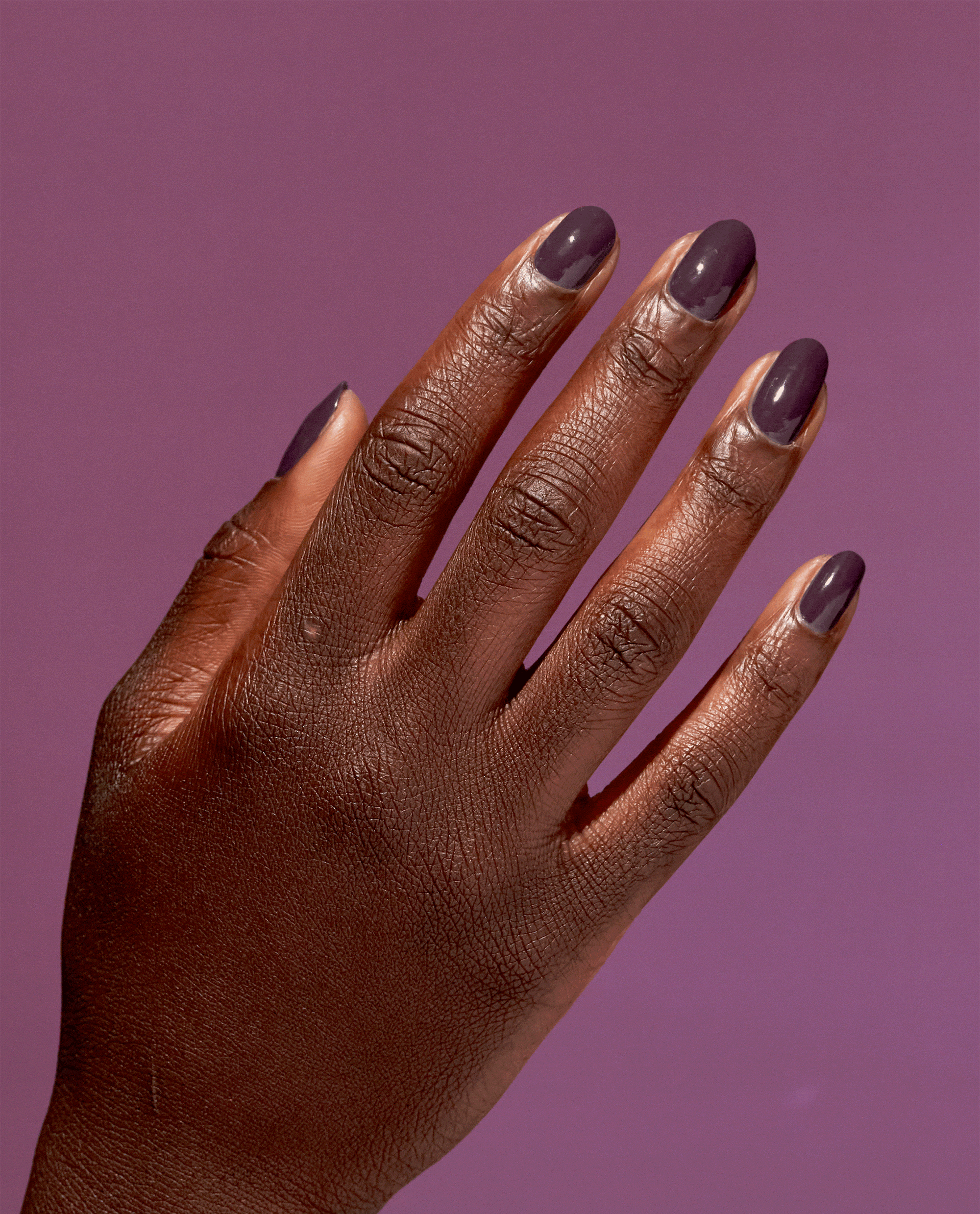 Hand modeling OPI Eco-Maniac Nature Strong Vegan Nail Lacquer, a glossy deep plum shade for fall nail colors, against a mauve purple background.