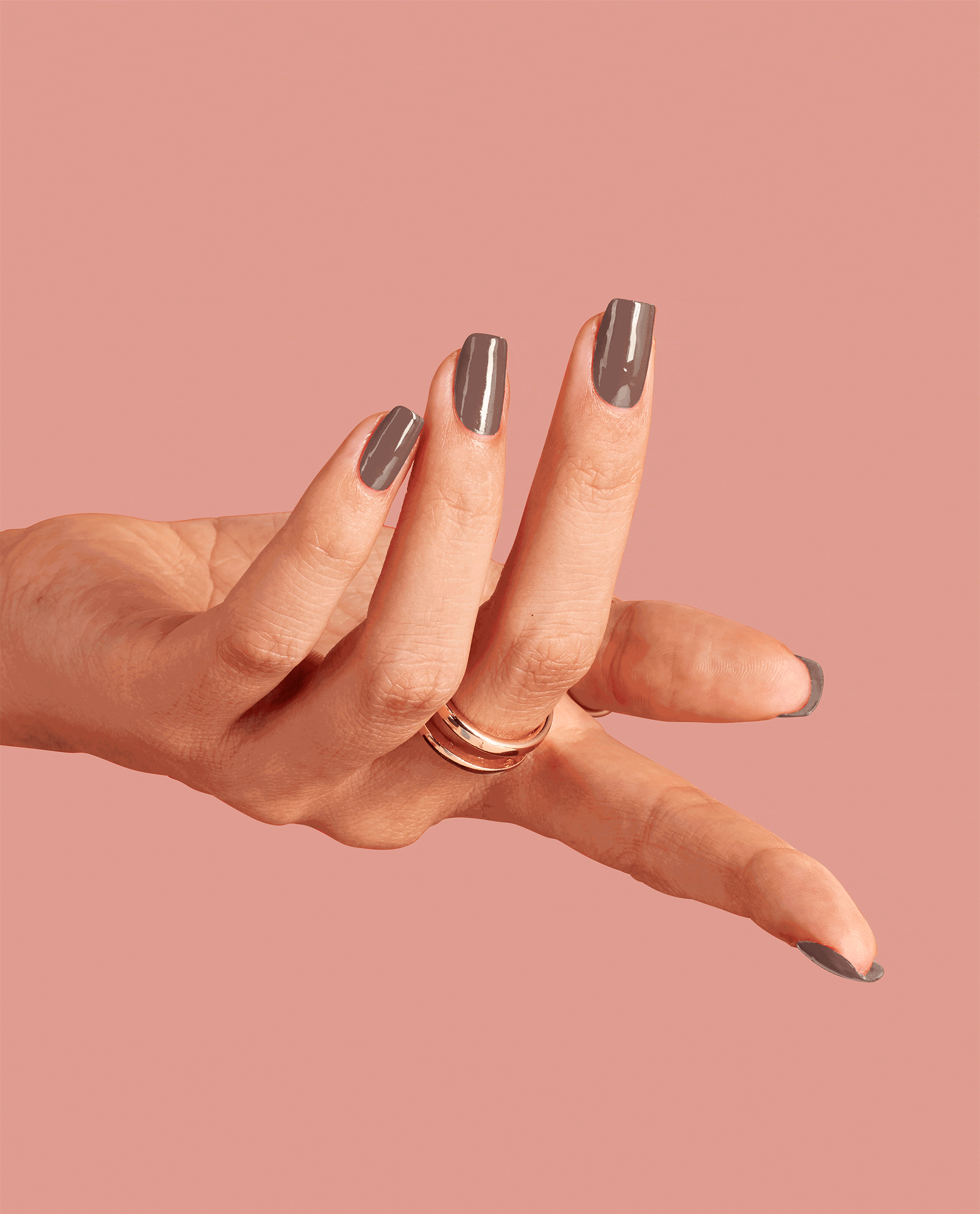 Hand modeling glossy taupe-brown OPI Espresso Your Inner Self nail lacquer, a chic fall nail color, with long squared nails and a gold ring against a soft pink background.
