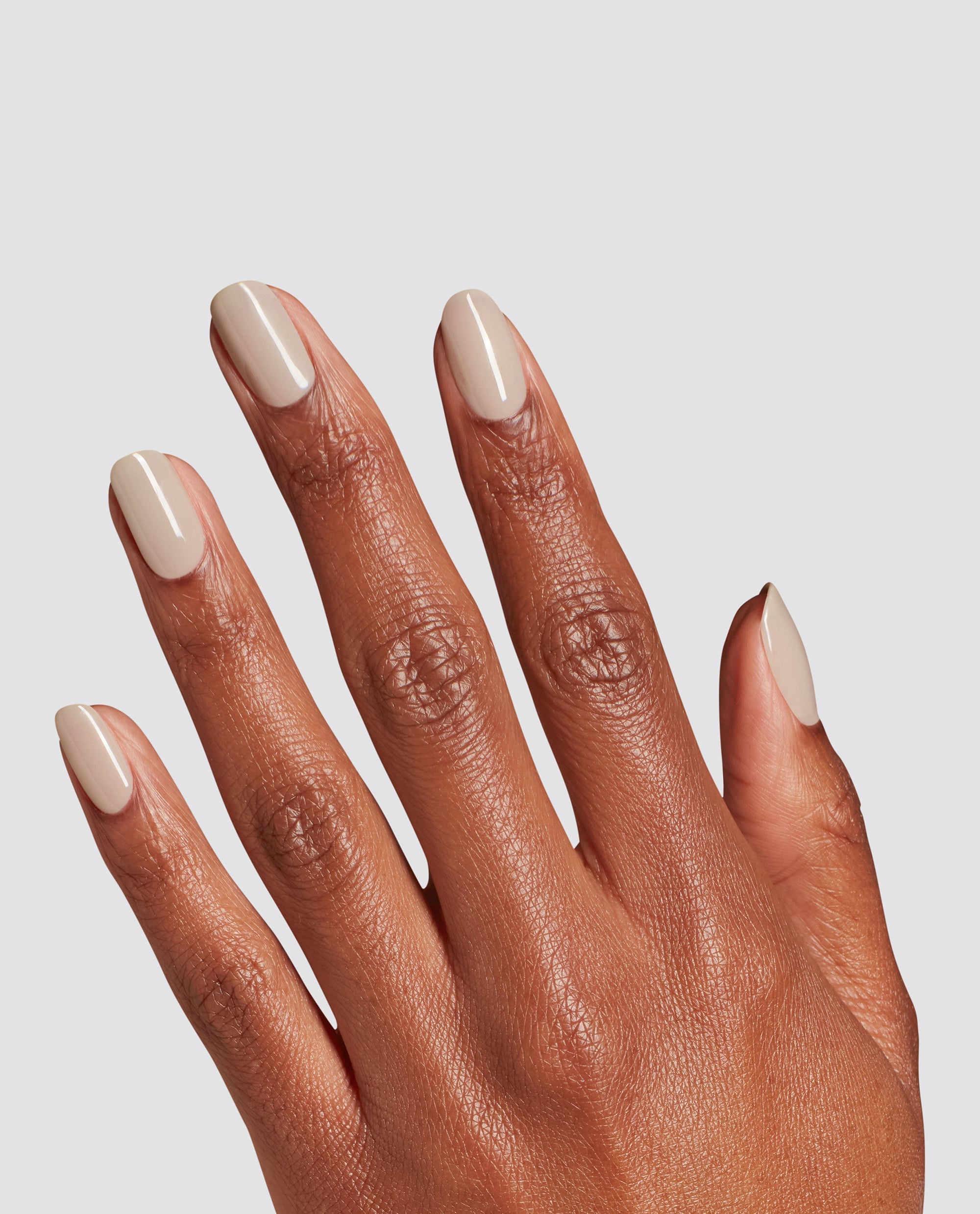 Hand displays glossy almond nails painted with OPI Espresso Martini Please at-home gel nail polish, a creamy beige neutral for fall nail colors, against a light gray background.