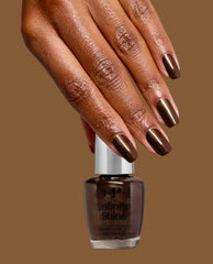 A hand with glossy espresso-brown metallic nails rests on an OPI Infinite Shine bottle in Espresso Your Style, showcasing rich fall nail colors against a warm brown background.