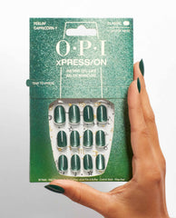 Hand with dark green almond nails holds OPI xPRESS/ON Feelin’ Capricorn-y press-on nails, showing emerald shimmer nails in glittery green packaging with zodiac accents.