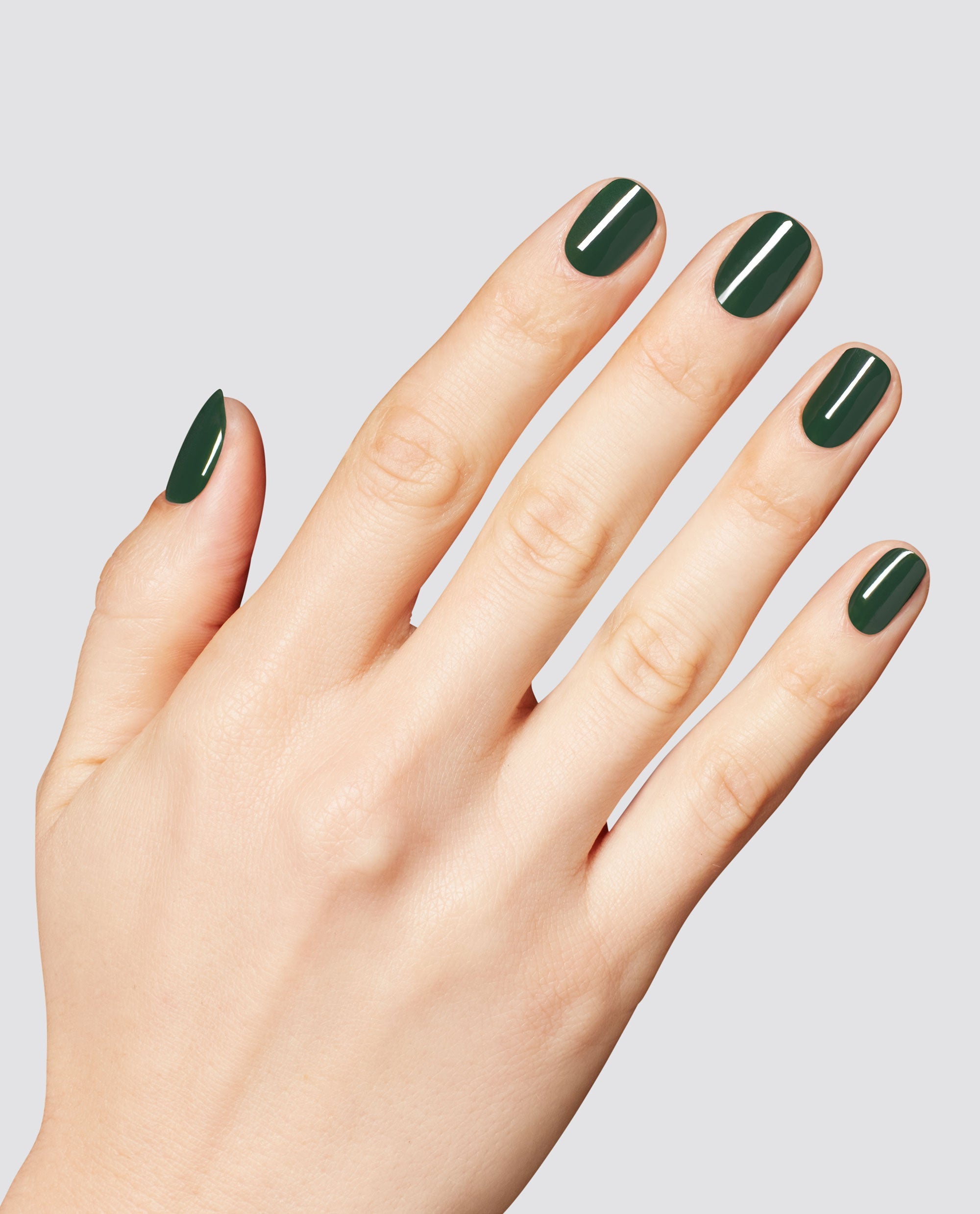 Hand displays glossy deep forest green nails in OPI Fir Surely Fast RapiDry polish, with a smooth manicure finish against a light gray studio background.