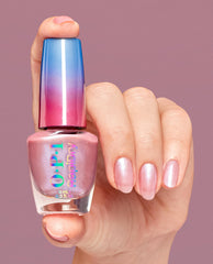 Hand with shimmery pink manicured nails holds an OPI Flash n’ Flirty RapiDry nail polish bottle with iridescent logo and blue-to-pink gradient cap against a mauve background, showcasing a stylish OPI nail polish gift set shade.