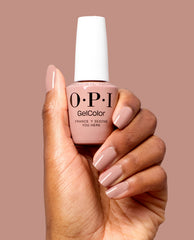 Hand with glossy blush nude nails holds OPI GelColor France-y Seeing You Here gel nail polish, a soft pink neutral shade for fall nail colors, against a muted mauve background.
