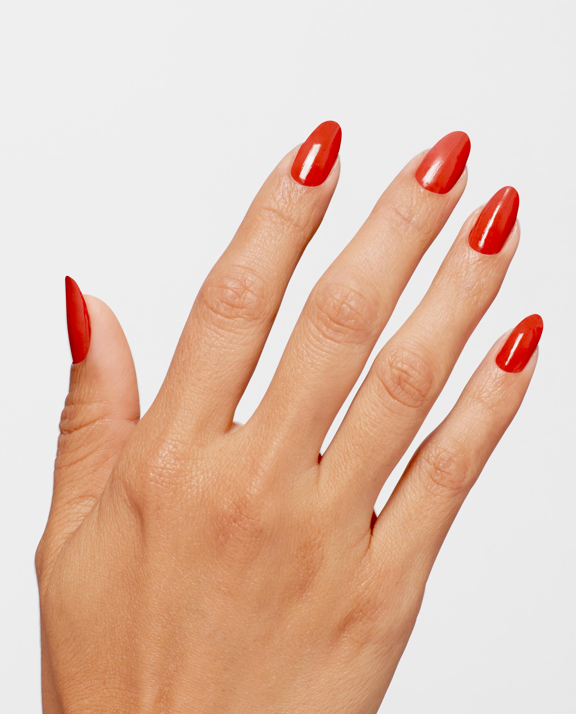 Hand modeling glossy almond nails painted OPI Full of Glambition Infinite Shine, a vibrant red-orange shade for fall nail colors, against a clean light gray background.