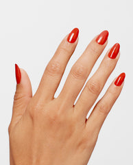 Hand modeling glossy almond nails painted OPI Full of Glambition Infinite Shine, a vibrant red-orange shade for fall nail colors, against a clean light gray background.
