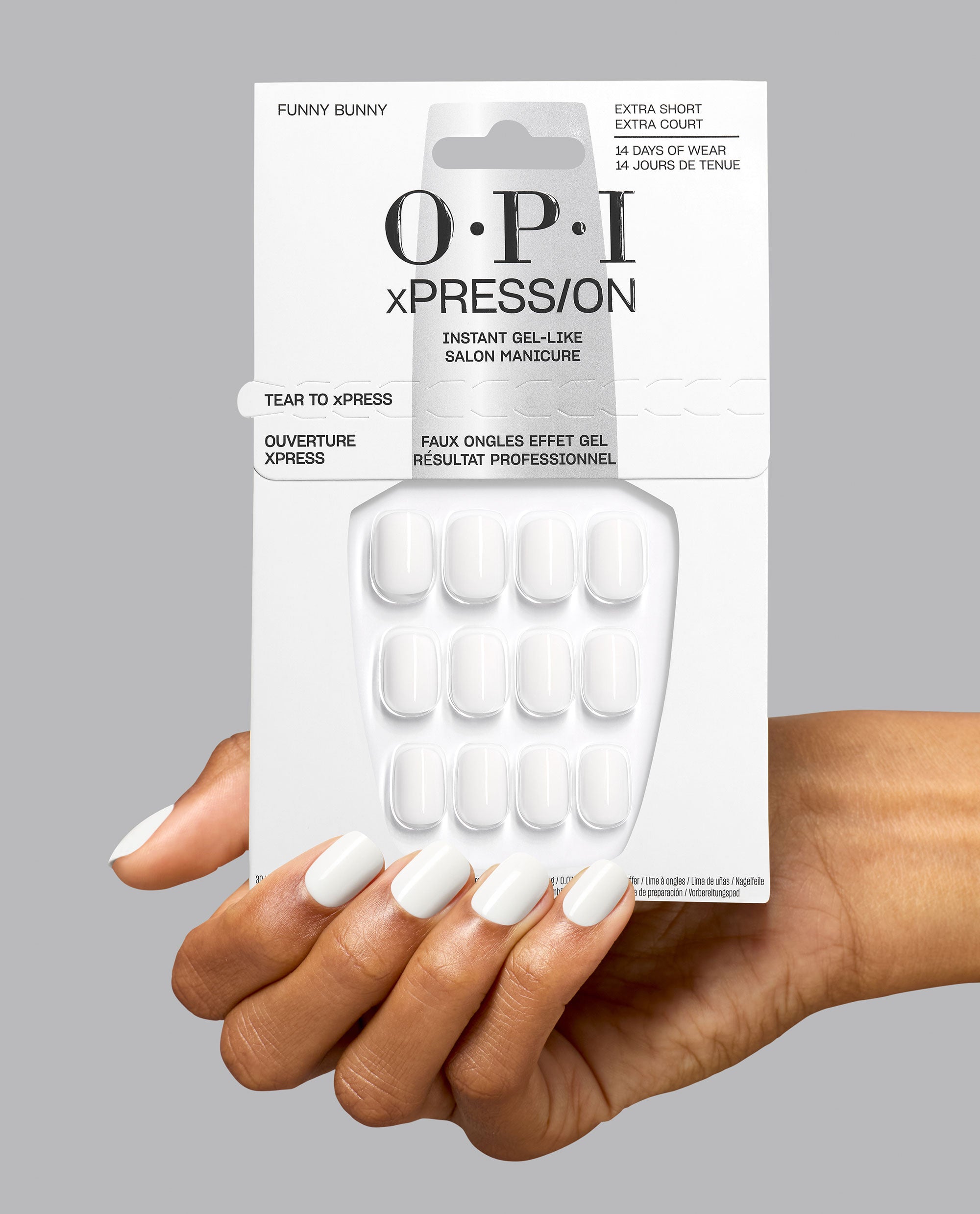 Hand holding OPI xPRESS/ON Funny Bunny extra short press-on nails, a soft white pick among fall nail colors, with gel-like packaging and matching glossy manicure on gray.