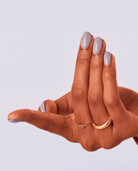 Hand with medium skin tone shows glossy pastel lavender Graffiti Sweetie OPI nail polish manicure, nails shaped oval and paired with delicate gold rings, against a clean light purple background showcasing the nail lacquer color and shine.