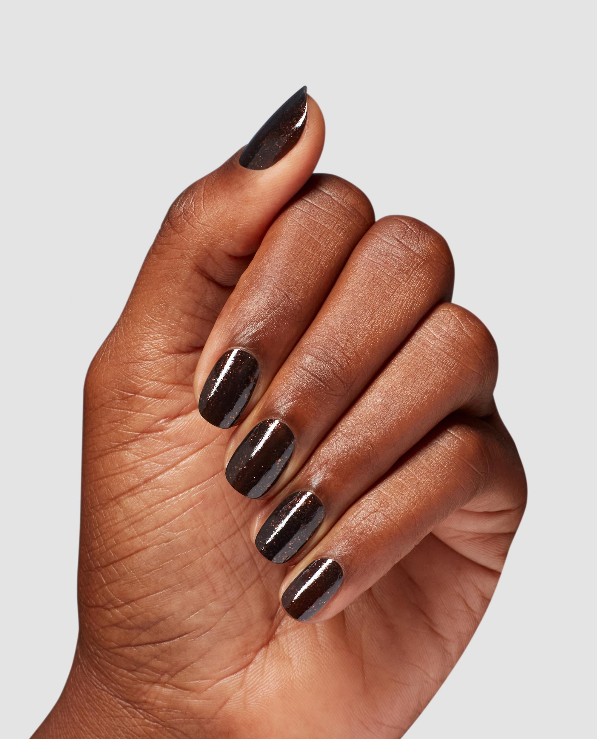 Hand showing short oval nails painted with Grunge Queen OPI nail polish, a deep espresso-brown nail lacquer with subtle shimmer, against a light gray background, highlighting the glossy, salon-quality finish for US manicure shoppers.