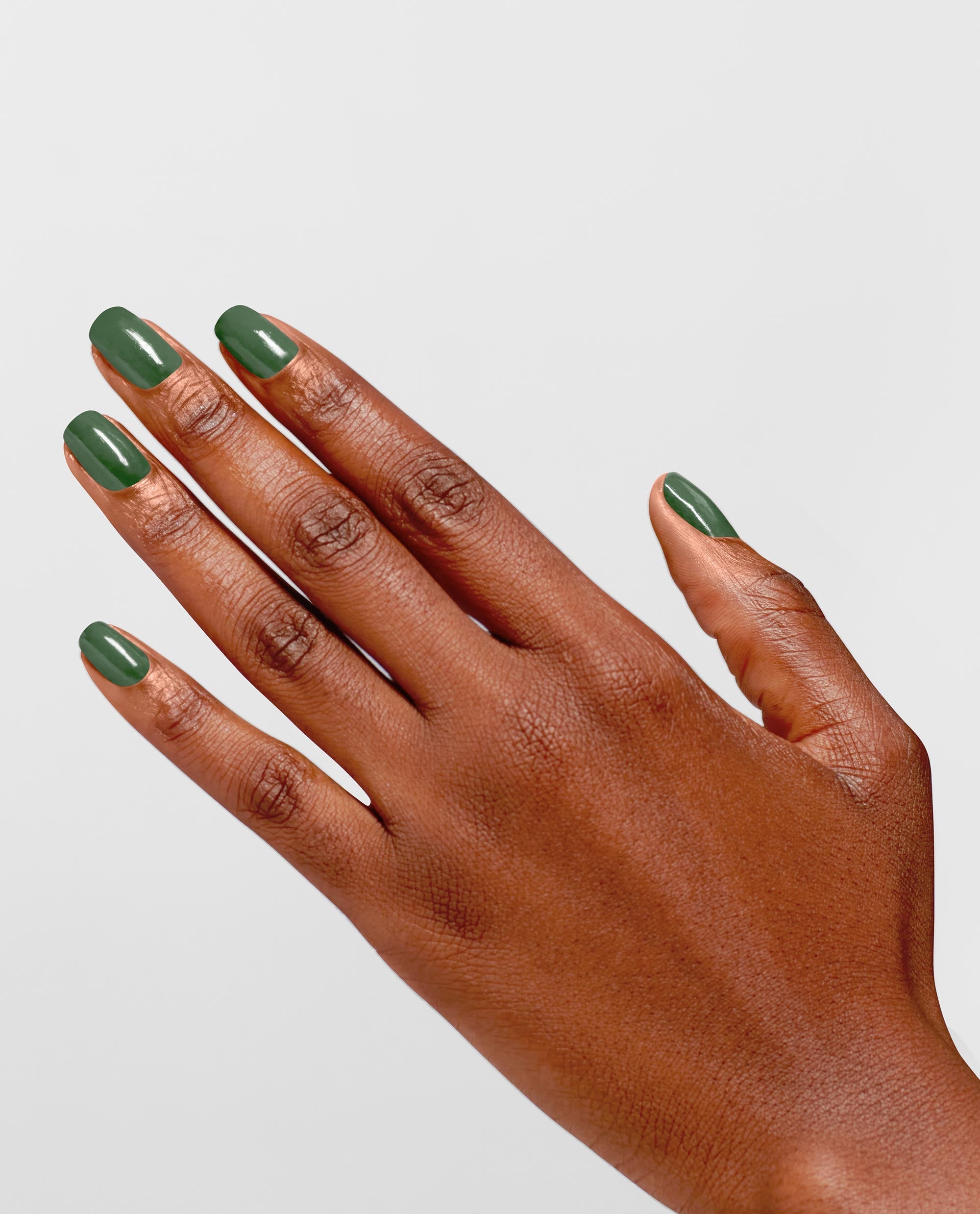 Hand with glossy evergreen manicure showcases OPI Infinite Shine Happily Evergreen After green nail polish on rounded nails, fingers splayed against a clean light gray background, highlighting a fresh pick for spring nail colors.
