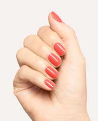 Hand displaying glossy coral-red Heat Vision nail lacquer on short rounded nails, a trending OPI manicure shade against a clean white studio background.