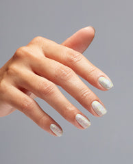 Hand with neatly manicured nails shows OPI nail polish shade I Cancer-tainly Shine, a silver holographic glitter nail lacquer sparkling under soft light against a plain gray background.