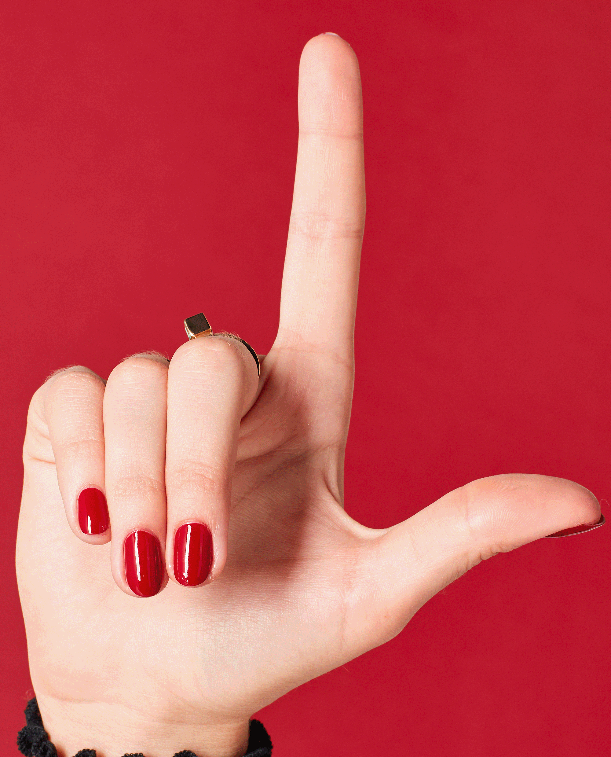 Hand with short, glossy red nails painted in OPI nail polish shade I Love You Just Be-Cusco held in an L shape against a matching red background, showcasing the vibrant nail lacquer color and smooth, even coverage.