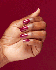 Hand displays glossy deep ruby red nails in OPI Infinite Shine I'm Not Really a Waitress, a shimmering choice for fall nail colors, against a matching red background.