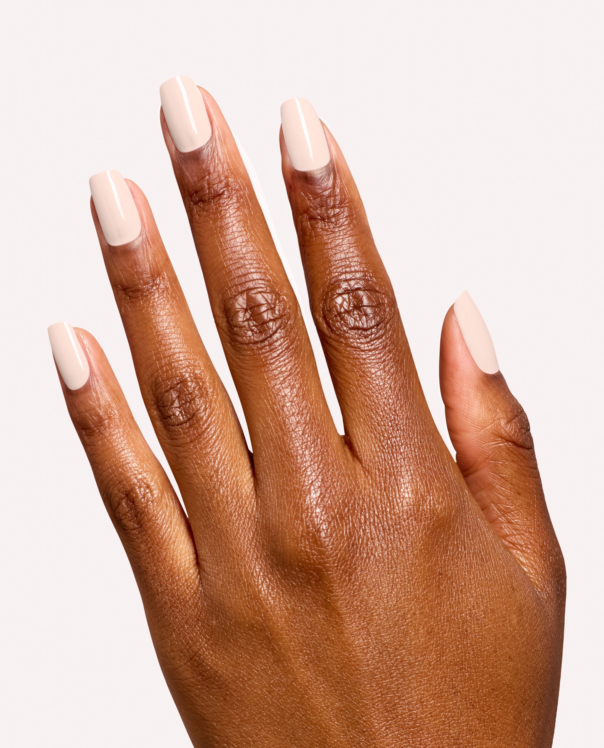 Hand modeling OPI Infinite Shine in I’m the Bossa Nova Now, a glossy pale beige fall nail color on short square nails against a clean white studio background.