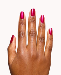 Hand displays glossy magenta OPI It’s All Greek to Me nail lacquer on short rounded nails against a white background, a vibrant pick for fall nail colors.