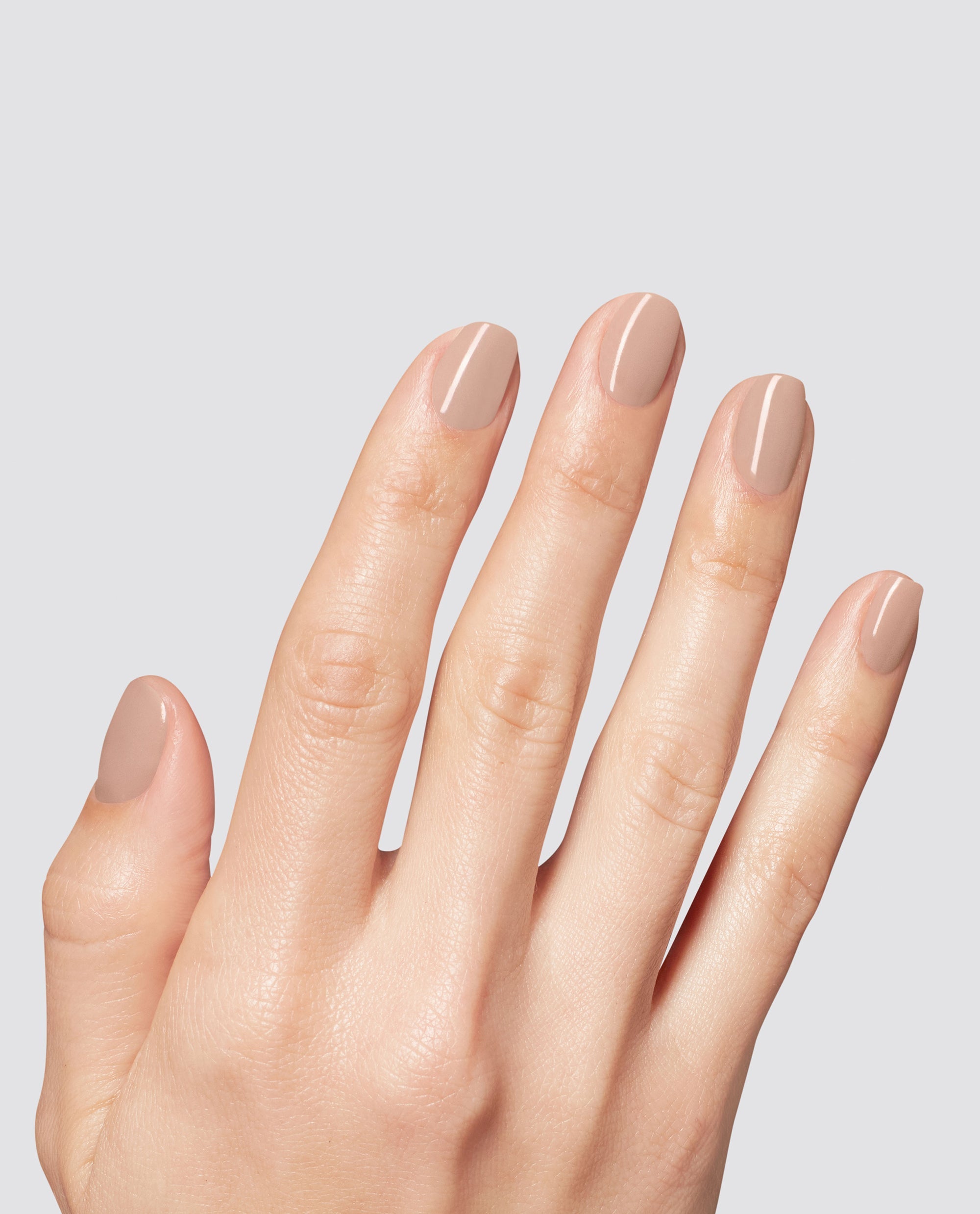 Hand modeling glossy nude beige Just Got Leid at-home gel nail polish on short rounded nails, an OPI-inspired neutral shade for fall nail colors against a light gray background.