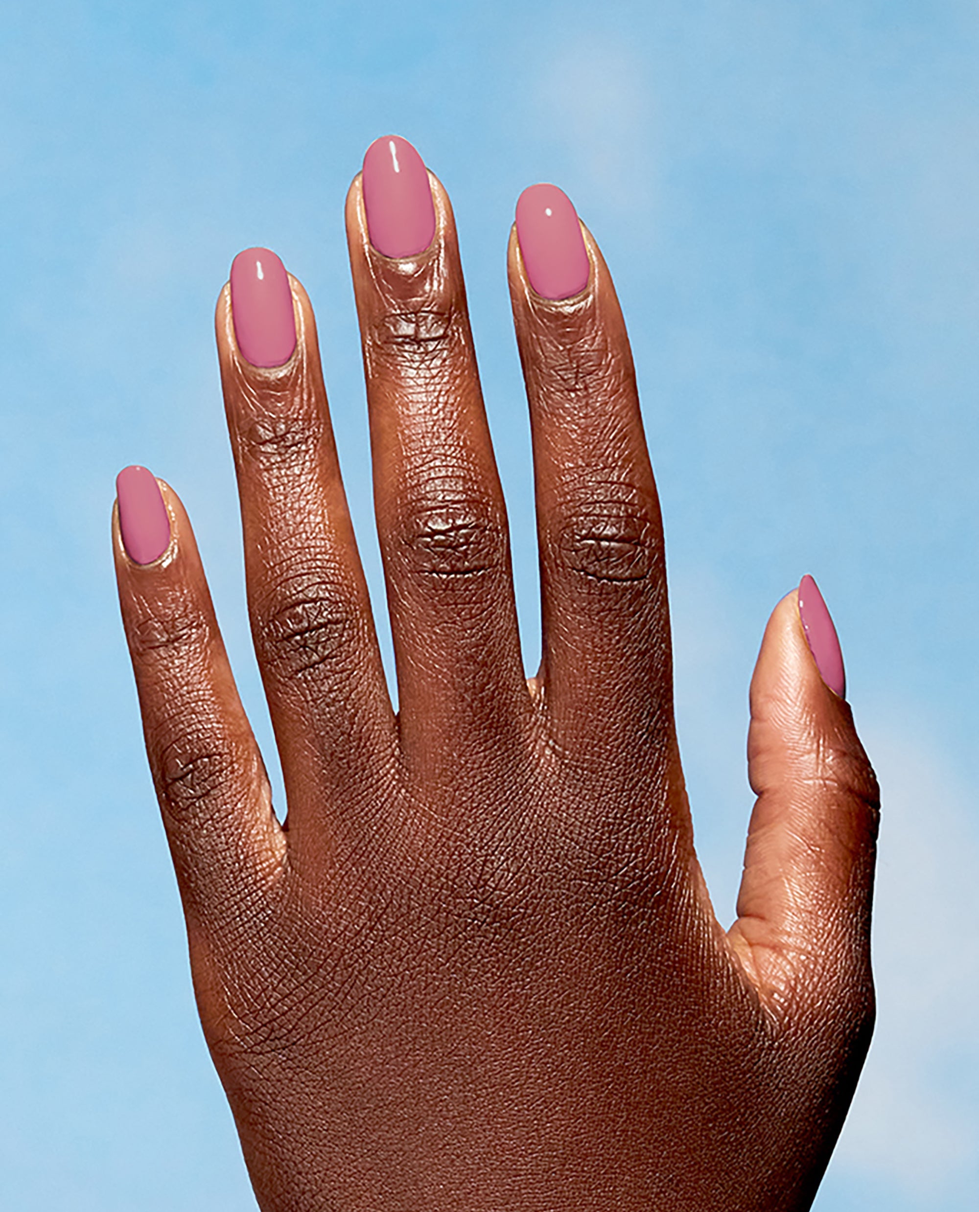 Hand with neatly manicured nails painted in Knowledge is Flower, a dusty rose shade from OPI Nature Strong Vegan Nail Lacquer, held against a soft blue sky background, ideal for showcasing an OPI nail polish gift set color option.