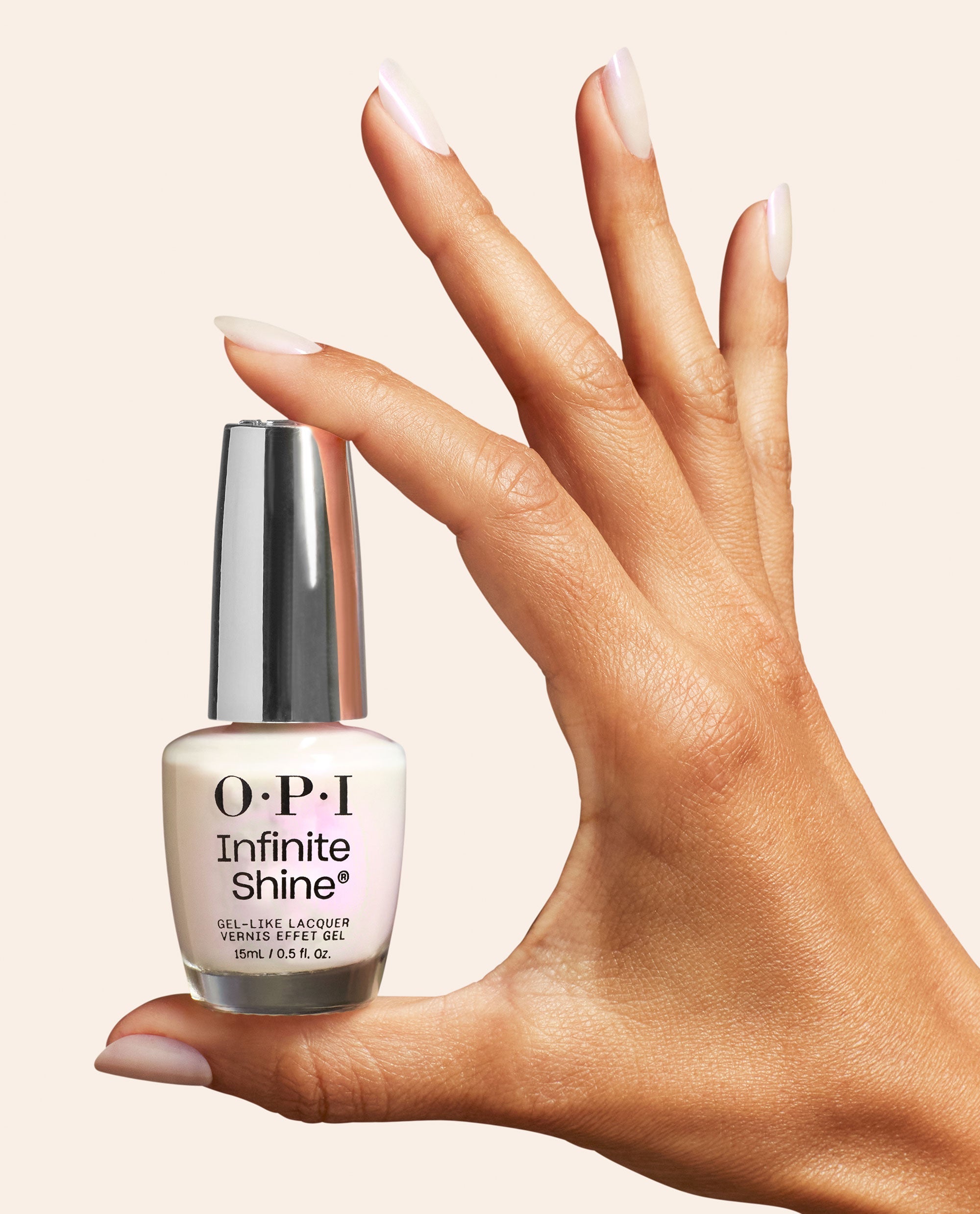 Hand with glossy almond-shaped nails holds OPI Infinite Shine Kyoto Oyster, a soft pearly white nail polish bottle with silver cap against a neutral beige background.
