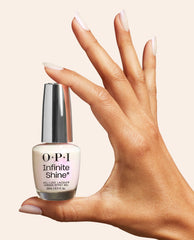 Hand with glossy almond-shaped nails holds OPI Infinite Shine Kyoto Oyster, a soft pearly white nail polish bottle with silver cap against a neutral beige background.