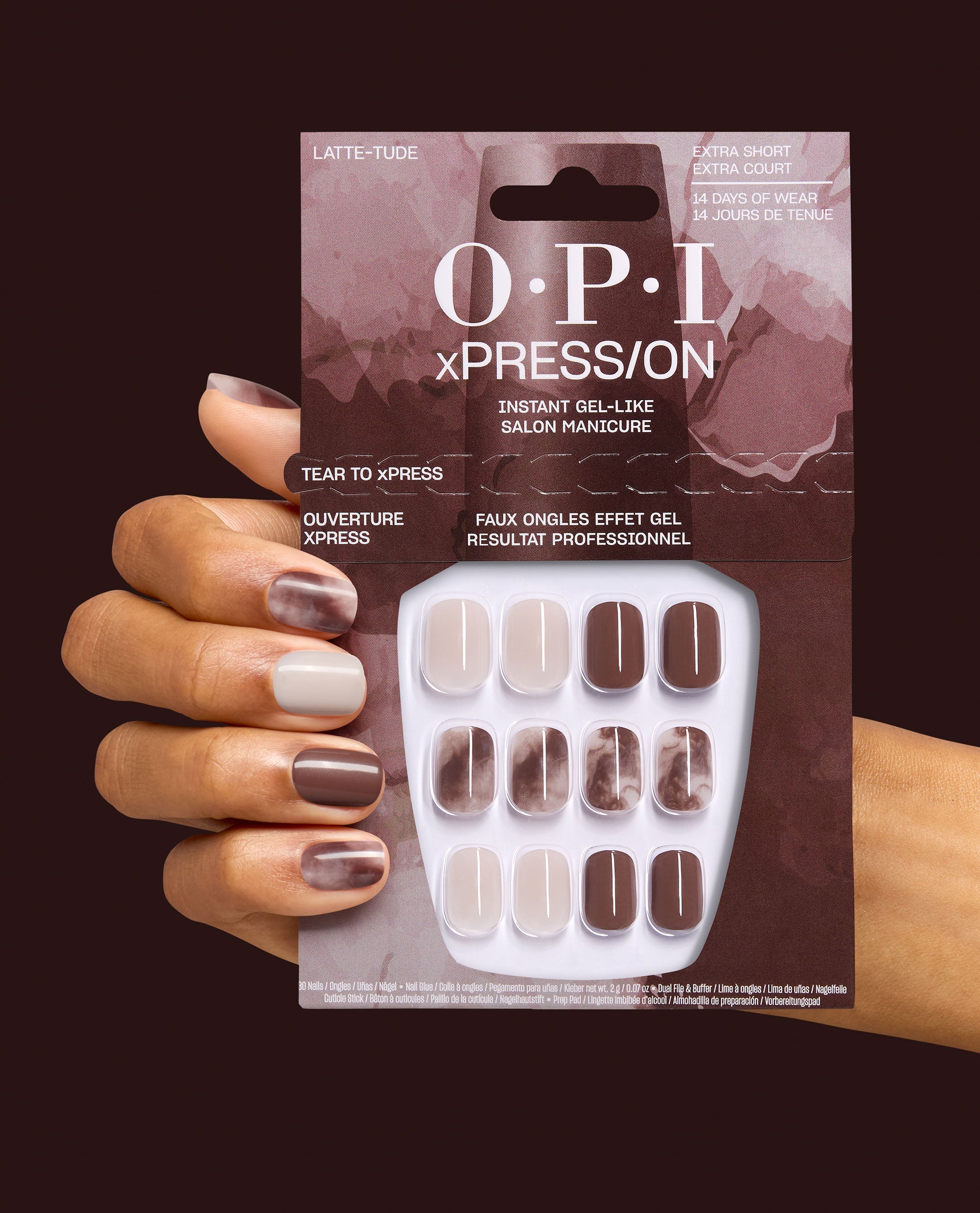 OPI xPRESS/ON Latte-tude press-on nails are held in packaging beside a manicured hand, showing extra-short beige, mocha brown, and marbled gel-like fall nail colors on a dark burgundy background.