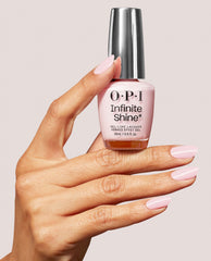 Hand with glossy pale lavender-pink nails holds an OPI Infinite Shine Lavender Bath gel-like lacquer bottle with a chrome cap against a soft neutral background.
