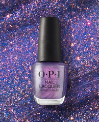 OPI nail polish bottle of Leonardo's Model Color nail lacquer standing upright, showcasing a shimmery purple metallic shade against a sparkling, glittery violet background.