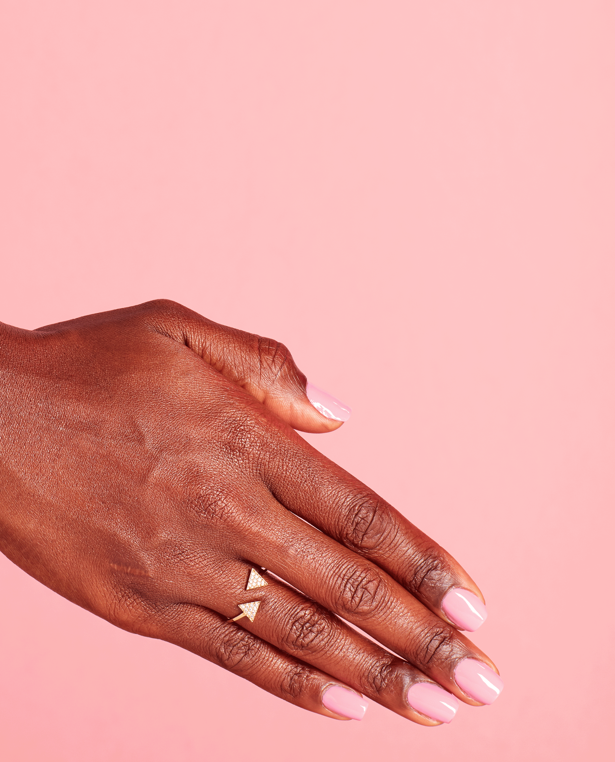 Well-groomed hand with short nails painted in Lima Tell You About This Color! pale pink OPI nail polish, resting against a solid pastel pink background, showcasing glossy nail lacquer and a delicate gold geometric ring.