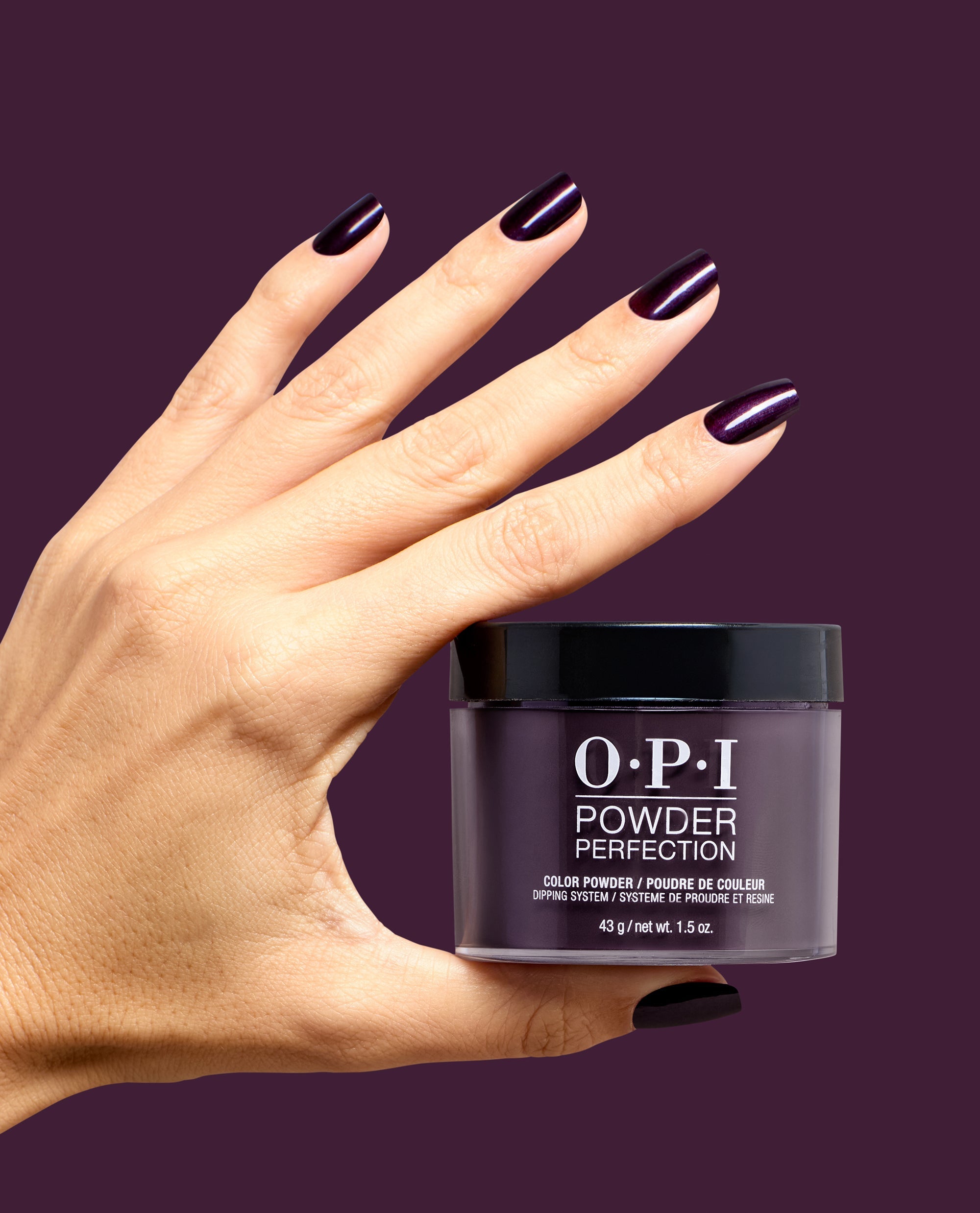 Hand with glossy deep plum nails holds OPI Powder Perfection Lincoln Park at Midnight dipping powder against a burgundy background, showcasing dark fall nail colors.