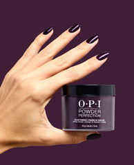 Hand with glossy deep plum nails holds OPI Powder Perfection Lincoln Park at Midnight dipping powder against a burgundy background, showcasing dark fall nail colors.