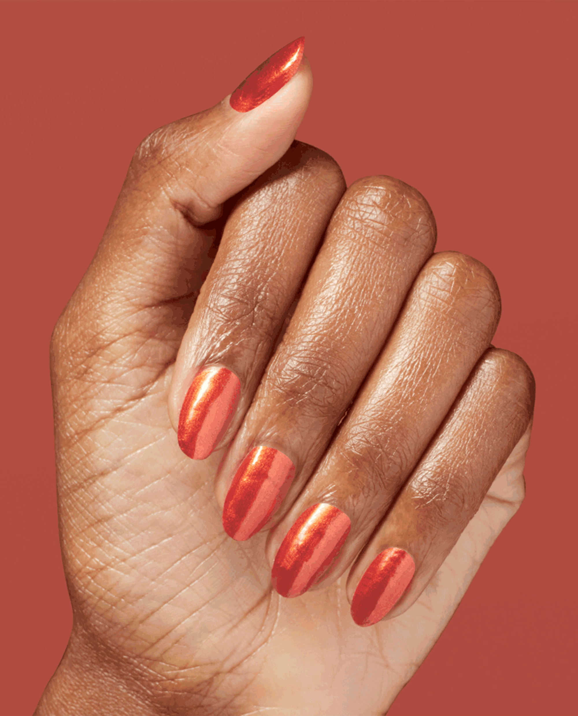 Hand with medium-length oval nails showcases Liquid Fire nail lacquer, a metallic fiery orange-red OPI nail polish, against a matching warm terracotta background for a bold, glossy manicure look.