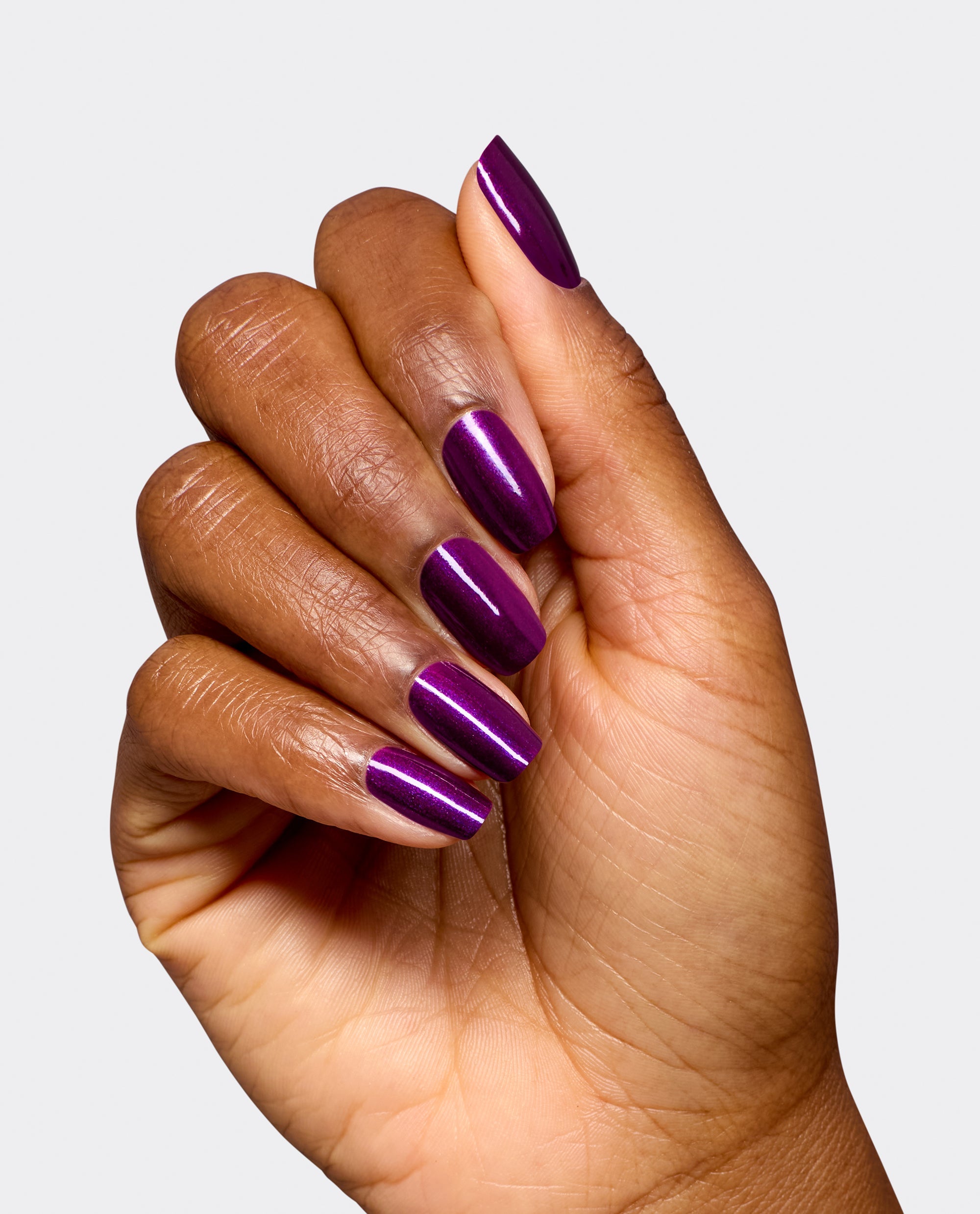 Hand modeling OPI Infinite Shine Louvre Me Lourve Me Not, a glossy deep purple shimmer manicure on long rounded nails against a light gray background, ideal for fall nail colors.