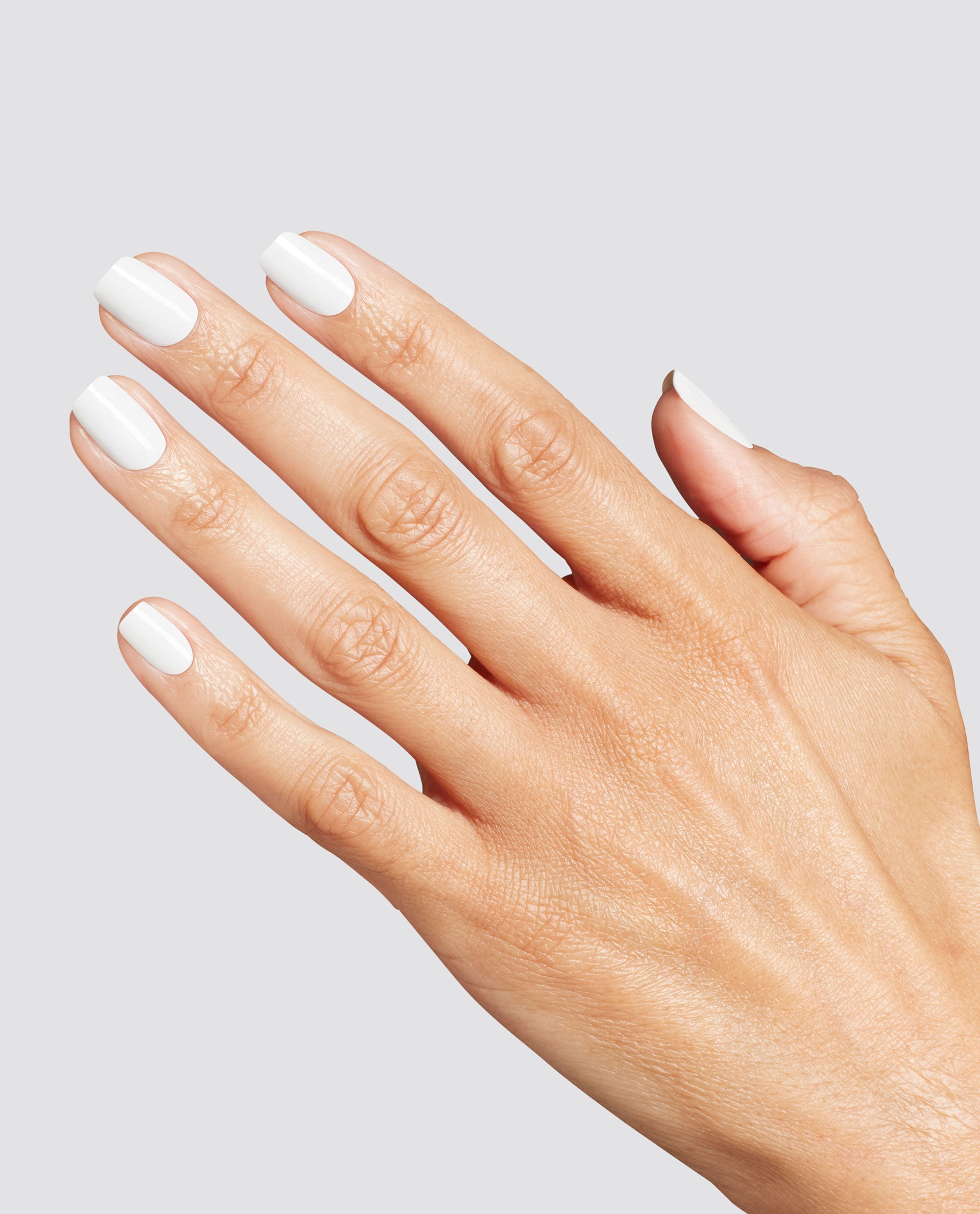 Hand with neatly manicured short nails painted in glossy opaque white, showcasing the OPI Love at Frost Sight RapiDry nail polish gift set finish against a clean light gray background.