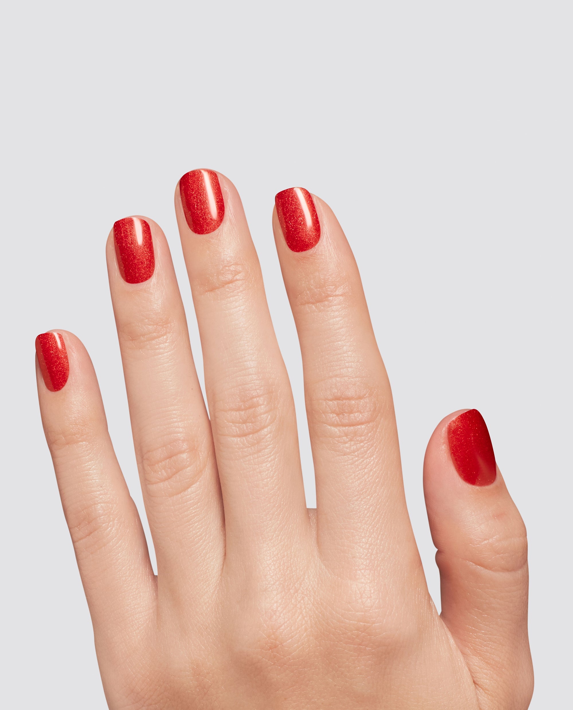 Fingernails display OPI Loves Me, Loves Me Hot at-home gel nail polish, a glossy red shimmer shade for fall nail colors, on a hand against a light gray background.