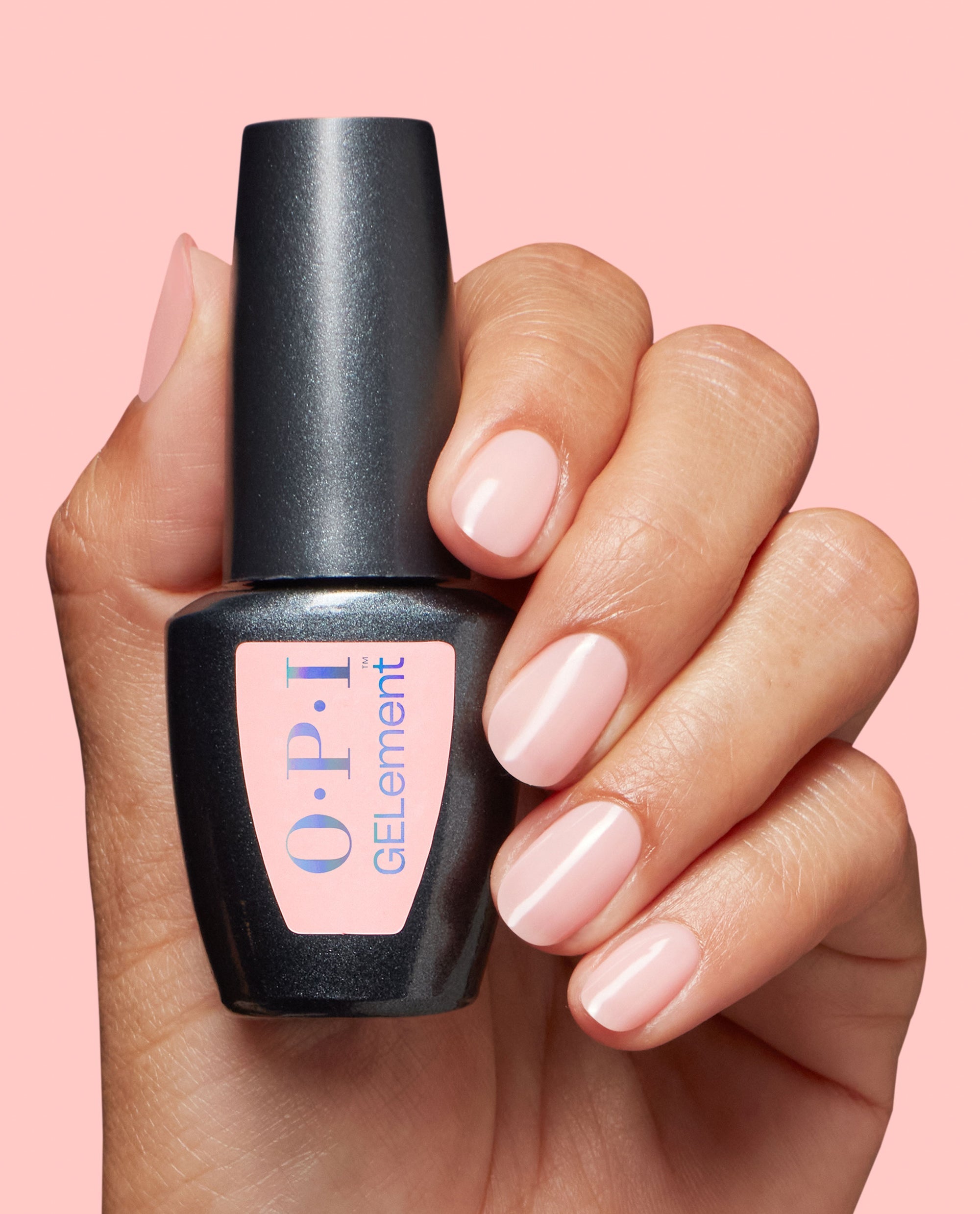 OPI Made Ya Blush at-home gel nail polish bottle held beside glossy pale blush pink manicured nails on a soft pink background, showcasing a trending sheer nude-pink gel shade.