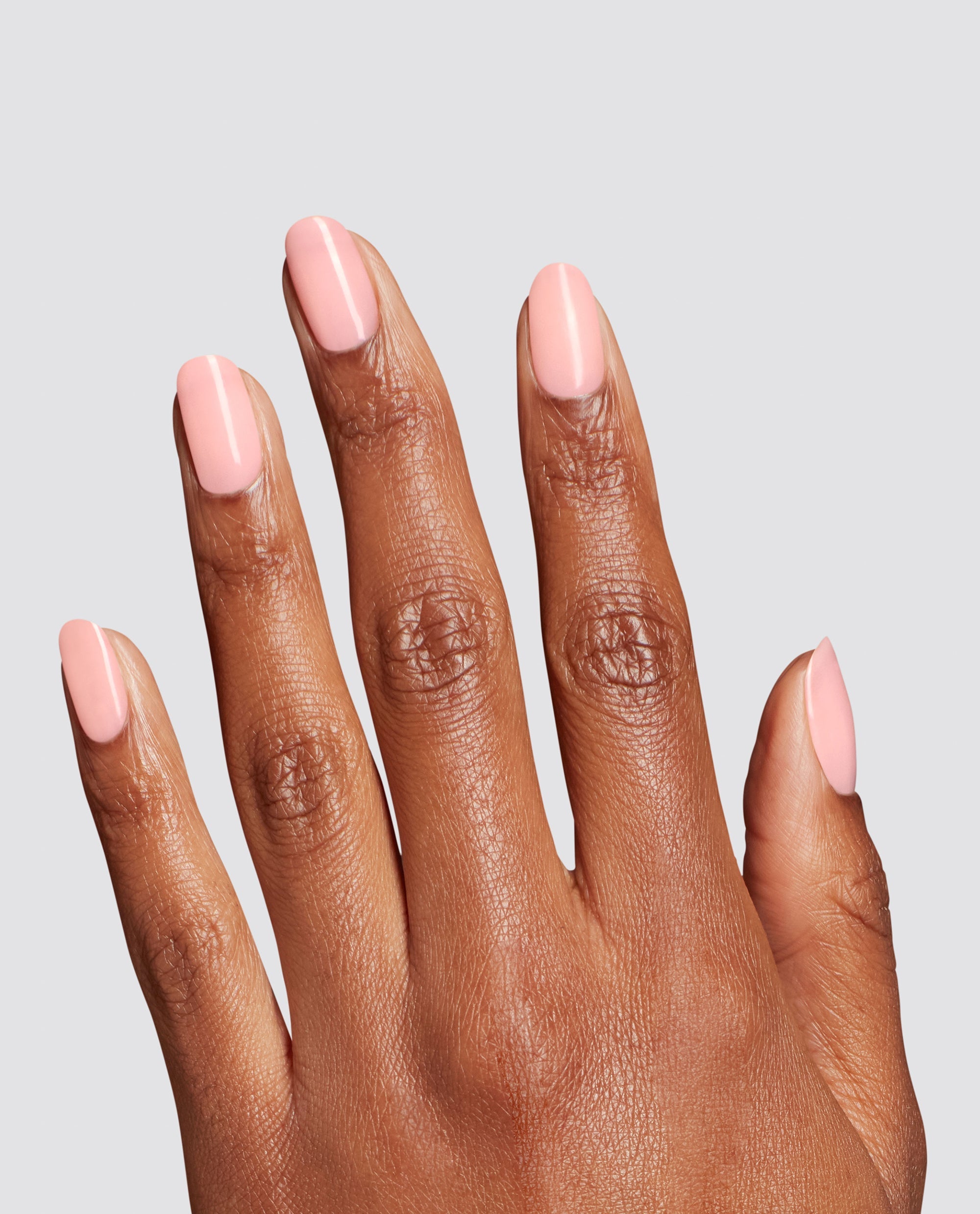 Hand modeling glossy pale pink Made Ya Blush at-home gel nail polish on short rounded nails, a trending OPI manicure shade against a clean light gray background.