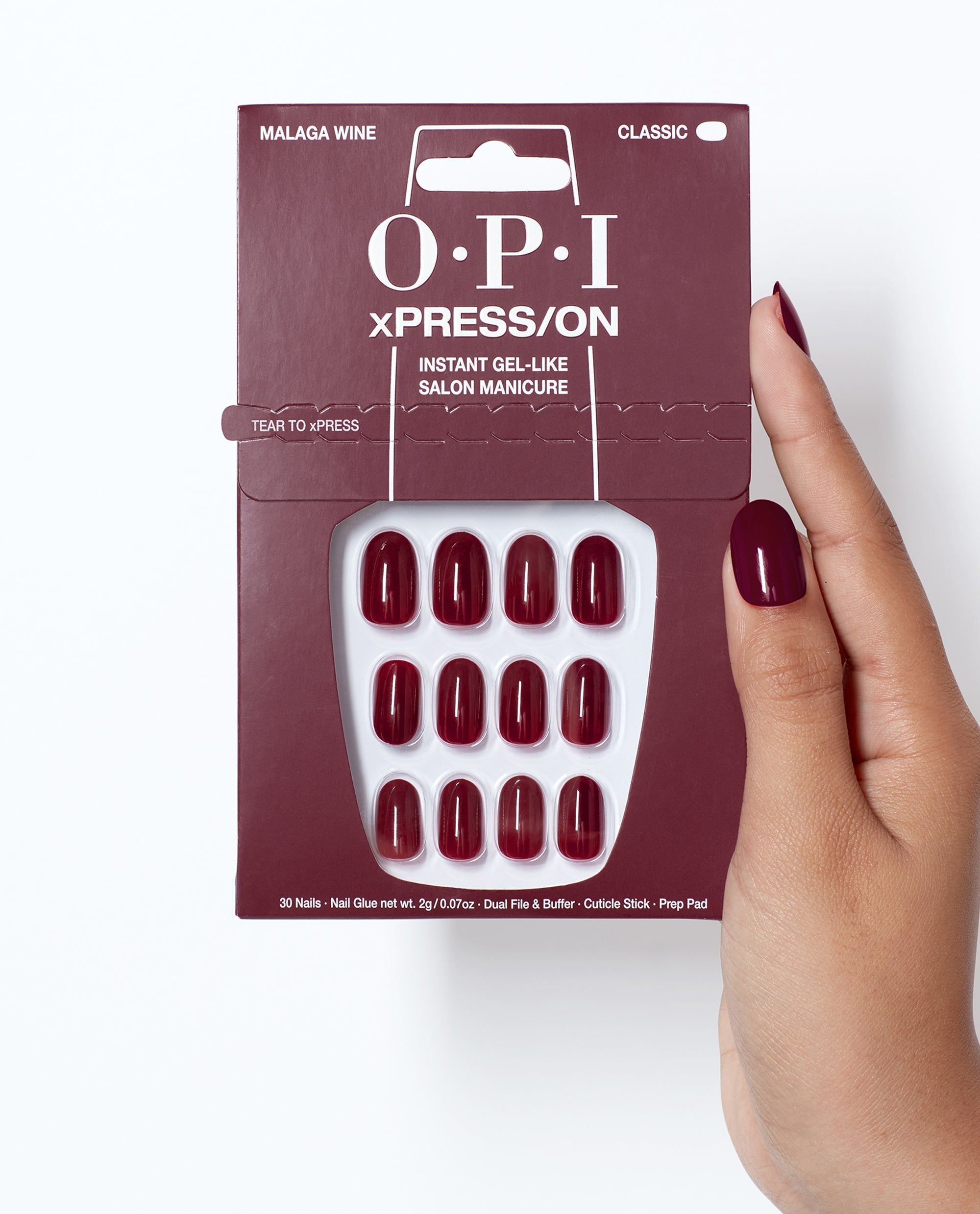 OPI Malaga Wine xPRESS/ON press-on nails in deep burgundy are displayed in classic packaging, held beside a matching manicure for rich fall nail colors.