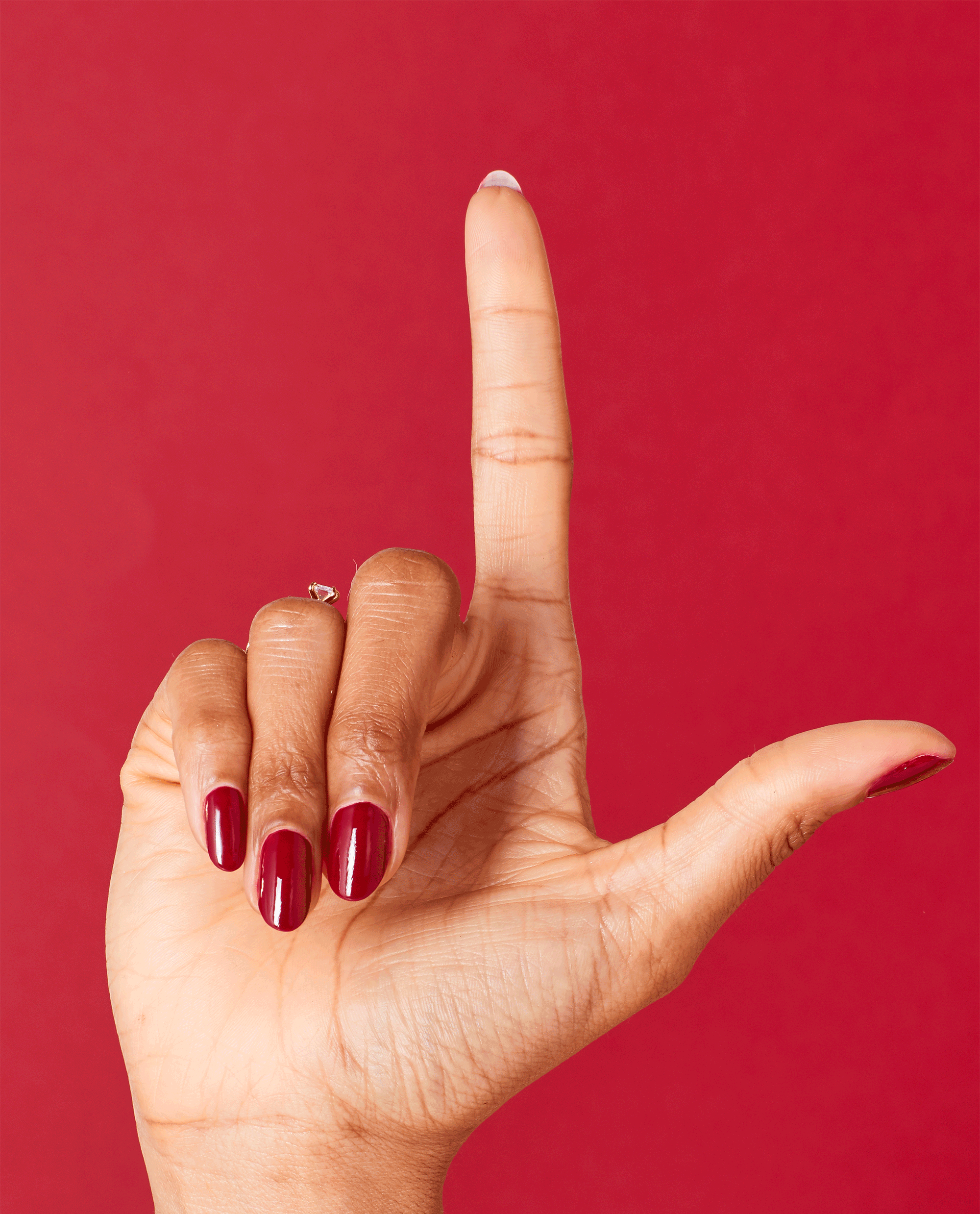 Hand with glossy deep wine red nails shows OPI Malaga Wine nail lacquer, a rich shade for fall nail colors, against a matching red background.