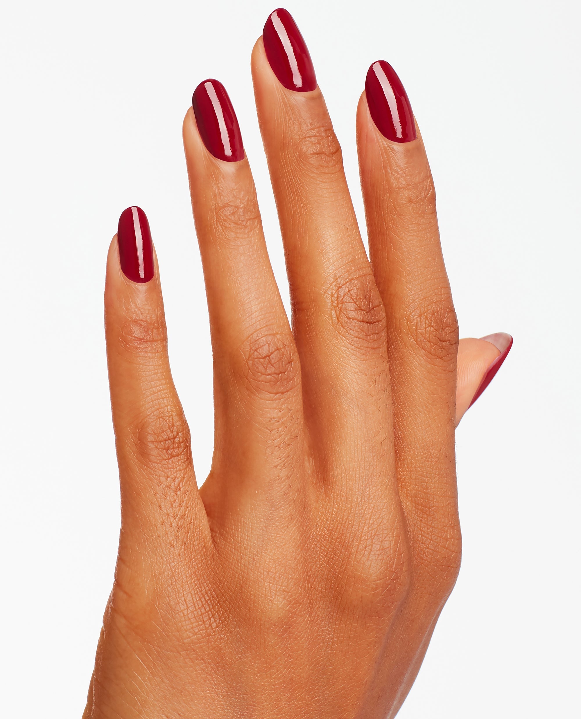 Hand modeling glossy deep red Malaga Wine nail lacquer on almond-shaped nails, showcasing OPI fall nail colors against a clean white background.
