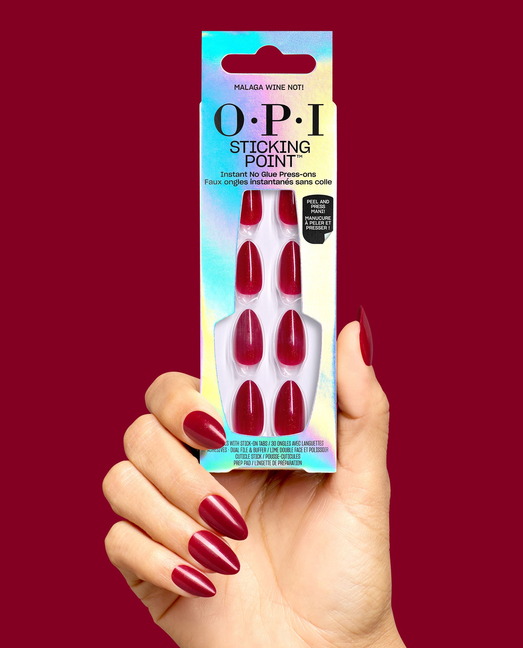 Hand holds OPI Sticking Point Malaga Wine Not press-on nails in iridescent packaging, showing glossy deep wine red almond nails against a burgundy background, ideal for fall nail colors.