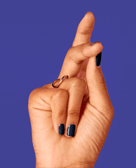 Hand with fingers crossed showing glossy deep navy Midnight Mantra nail lacquer, resembling a dark midnight blue OPI nail polish shade, against a bold purple background with a minimalist gold infinity ring accenting the look.