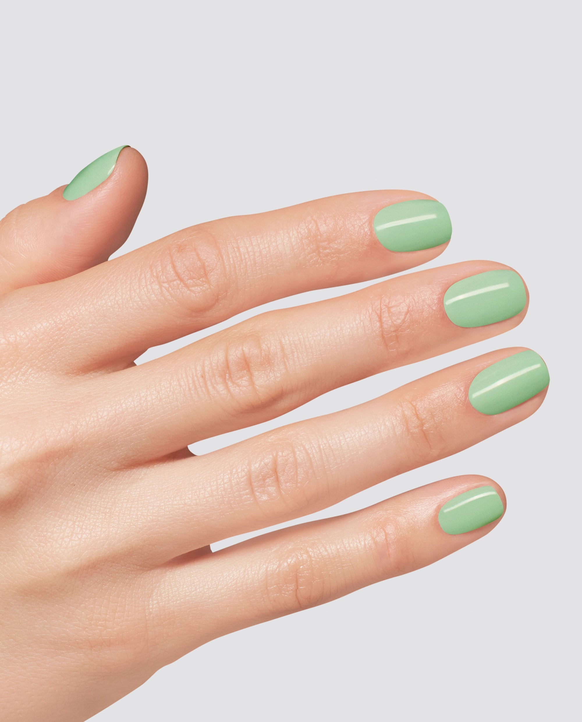 Hand modeling glossy mint green OPI Mint to Be at-home gel nail polish on short rounded nails against a light gray studio background.