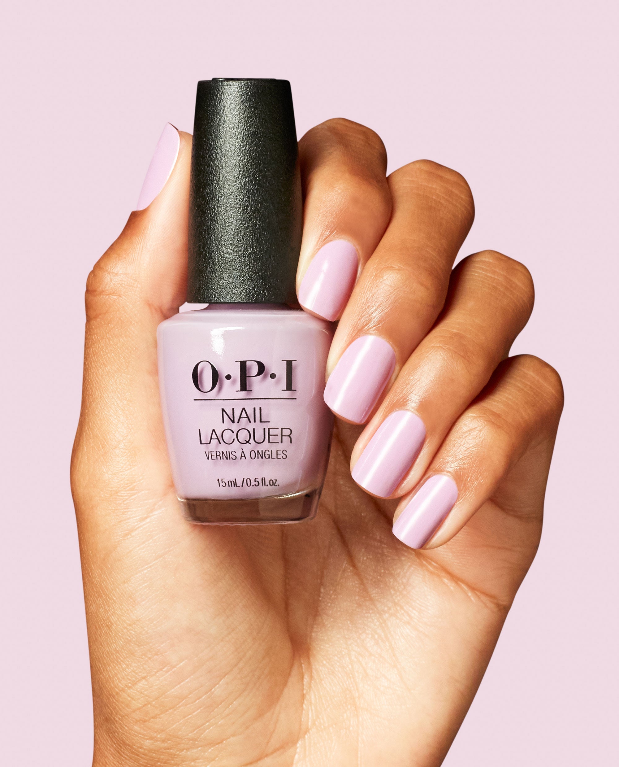 OPI Mod About Me Nail Lacquer bottle in soft pastel pink held by a hand with matching glossy pink manicured nails against a light pink background.