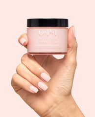 Hand with pale pink manicured nails holds OPI Powder Perfection Mod About You Pastel dipping powder jar, a soft blush shade for OPI fall nail colors, on a light pink background.