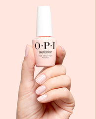 Hand holding OPI GelColor Mod About You Pastel gel nail polish with glossy pale pink manicured nails against a soft blush background, a delicate OPI shade for fall nail colors.
