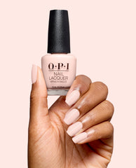 Hand with glossy pale pink nails holds OPI Mod About You Pastel Nail Lacquer, a soft blush shade for fall nail colors, against a light pink studio background.