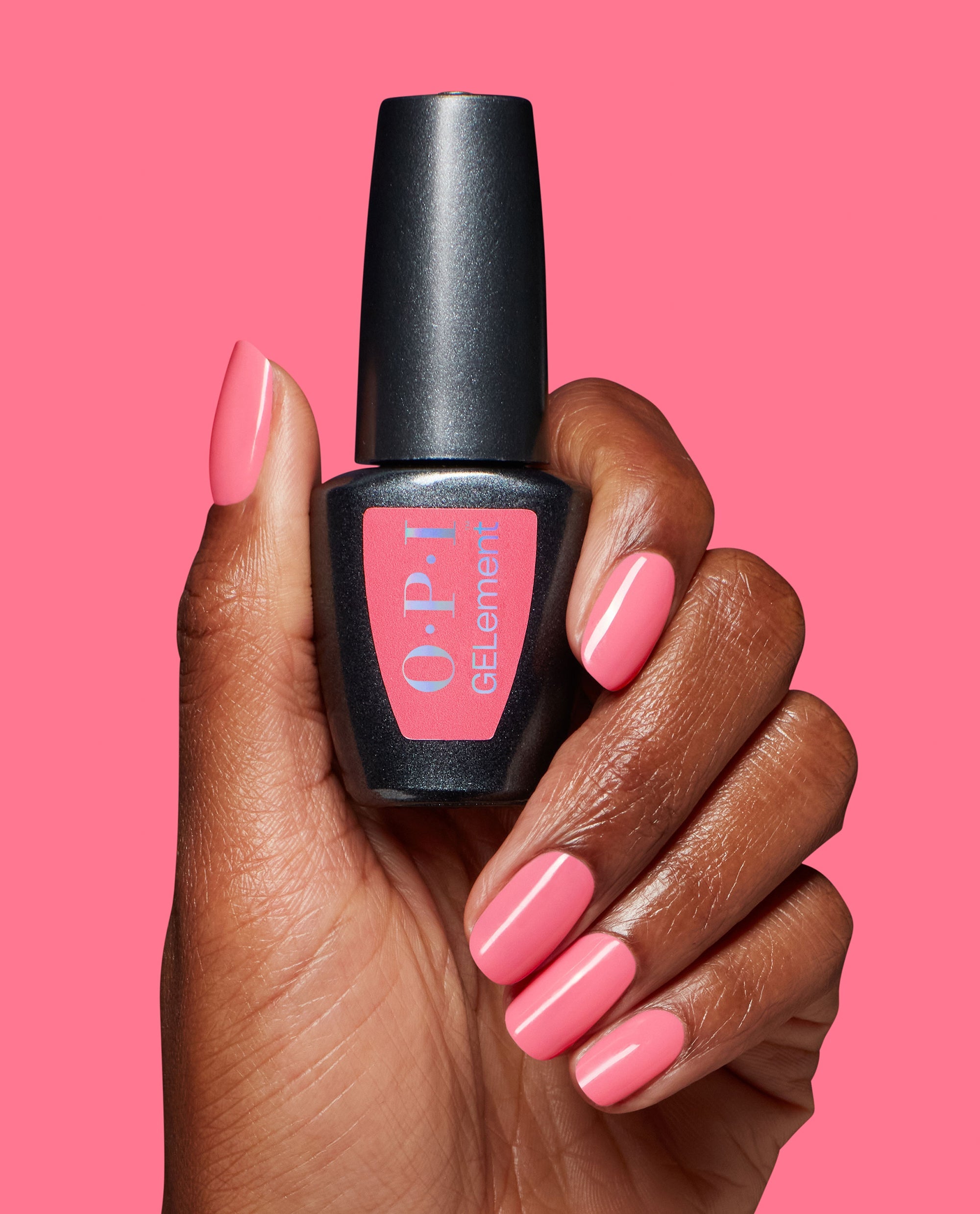 Hand with glossy pink MVPink at-home gel manicure holding an OPI GELElement bottle against a matching pink background, showcasing the OPI nail polish gift set color and shine.