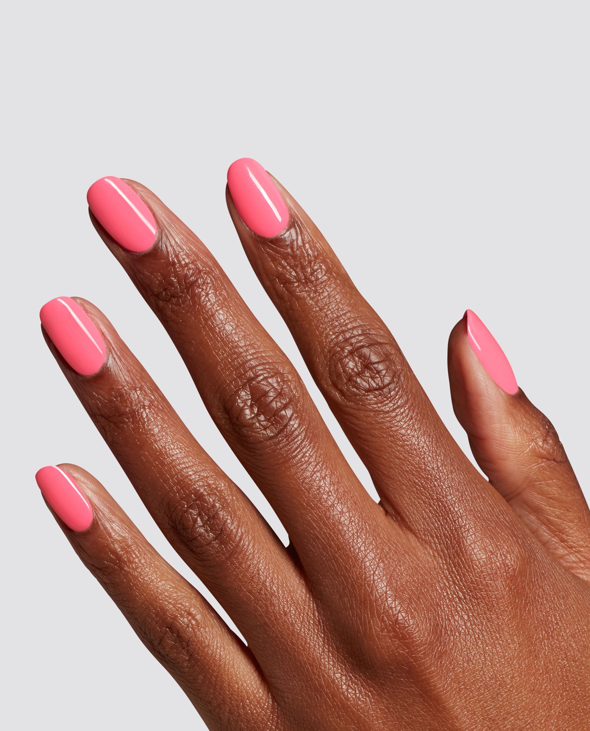 Hand with neatly manicured nails shows bright bubblegum pink MVPink at-home gel nail polish, resembling an OPI shade, against a plain gray background, ideal for a modern nail polish gift set look.