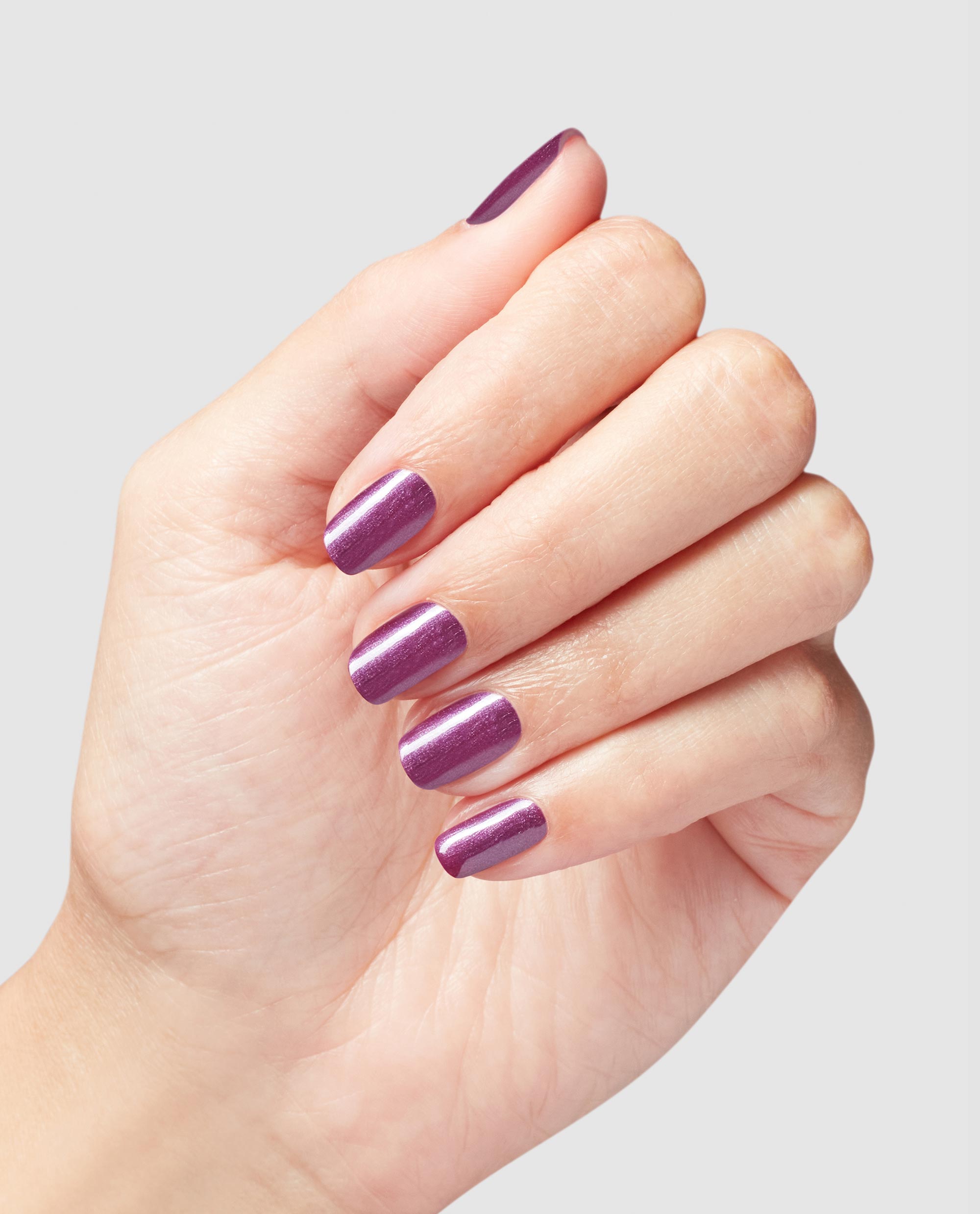 Hand modeling OPI Infinite Shine My Berry Janes, a glossy shimmering berry-purple manicure on short rounded nails against a light gray background, ideal for fall nail colors.