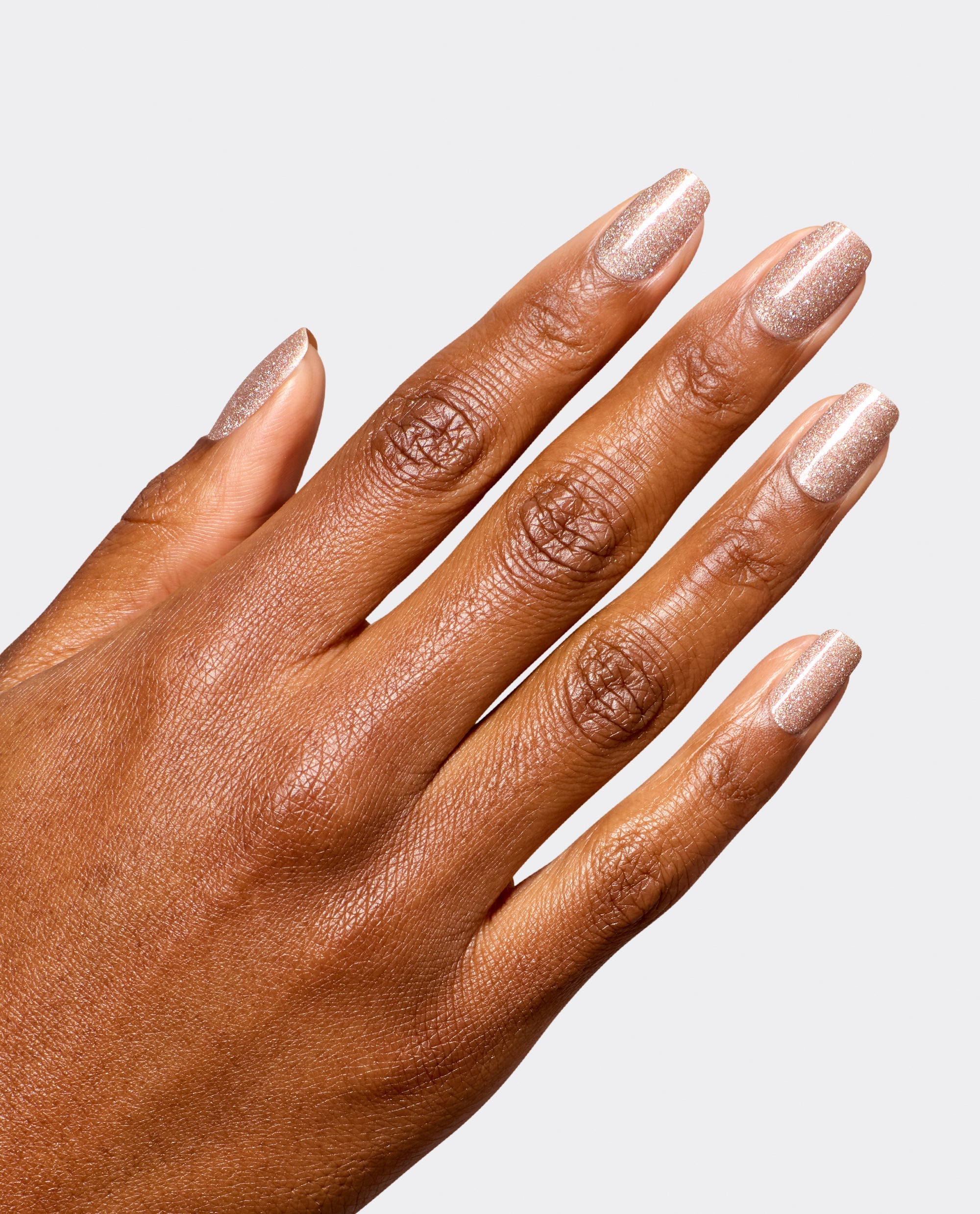 Hand modeling OPI Infinite Shine My Private Yacht, a sparkling champagne taupe manicure with glossy shimmer, shown on medium-brown skin against a light gray background for fall nail colors.